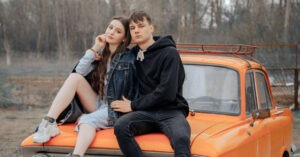 жінка і чоловік сидять на капоті помаранчевої машини