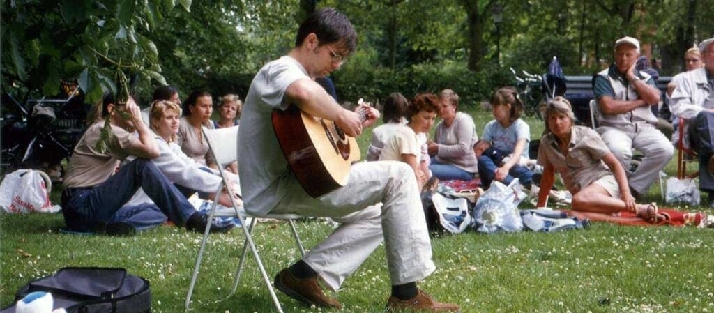 människor sitter på gräset kring en gitarrist som sitter på en stol