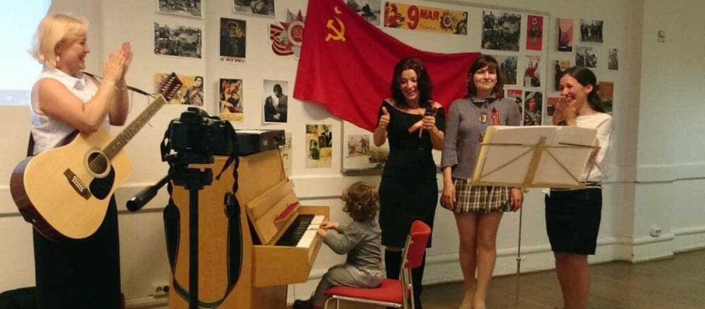 sjungande glada människor framför en vägg dekorerad med sovjetiska foton och flaggor från andra världskriget