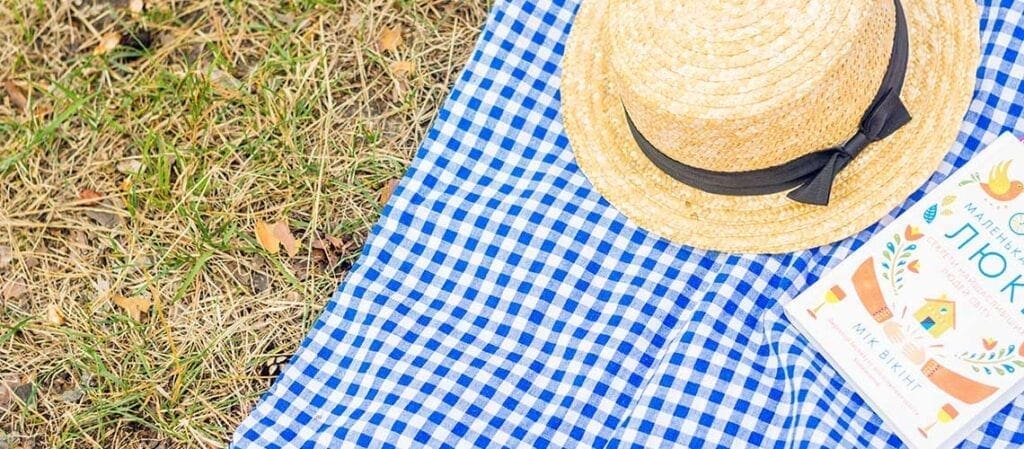 одеяло на траве со шляпой и книгой