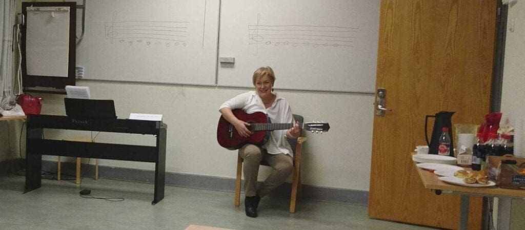sjungande och gitarrspelande kvinna som sitter på en stol framför en whiteboard