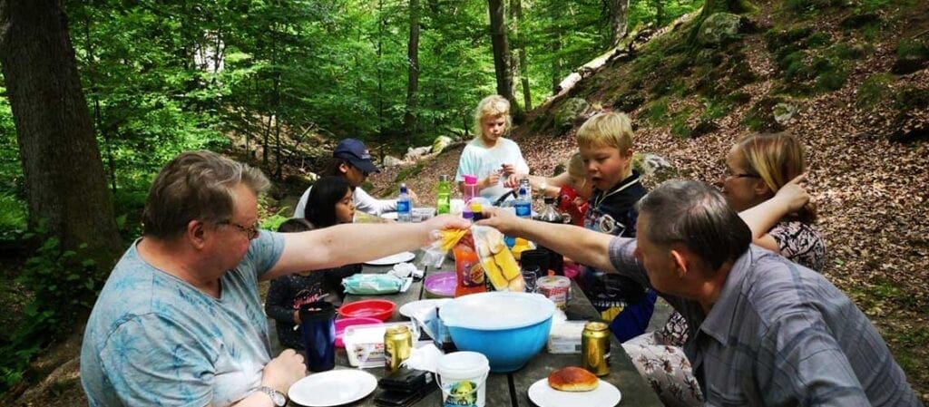 vuxna och barn i skogen vid ett bord med mat