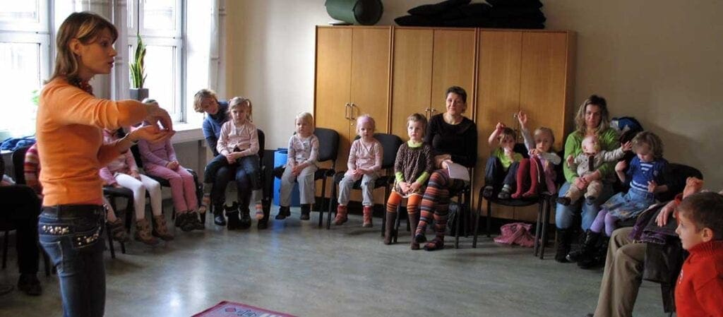kvinna som står upp framför barn och vuxna som sitter på stolar i en halvcirkel