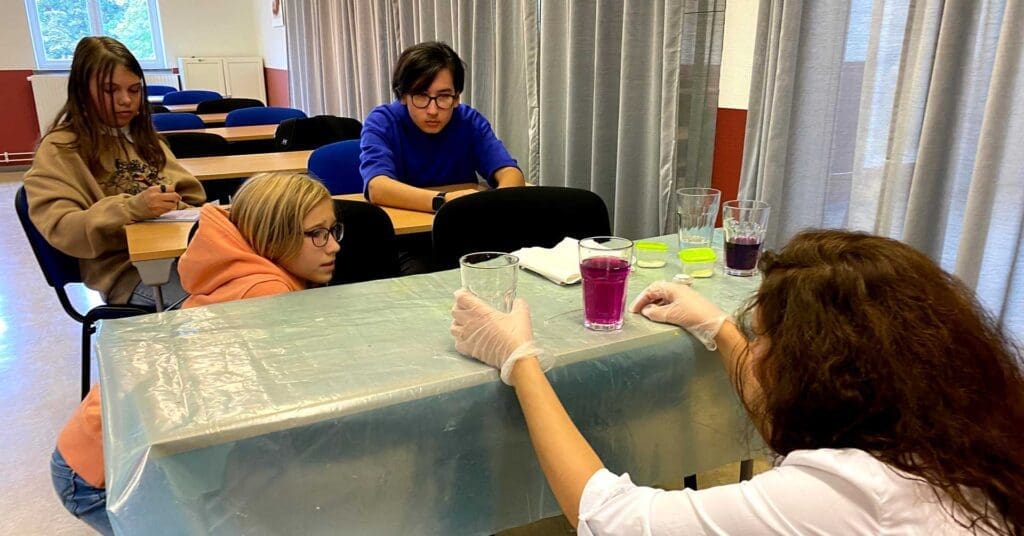 barn och lärare vid ett bord på vilket det står glas med vätskor i olika färger