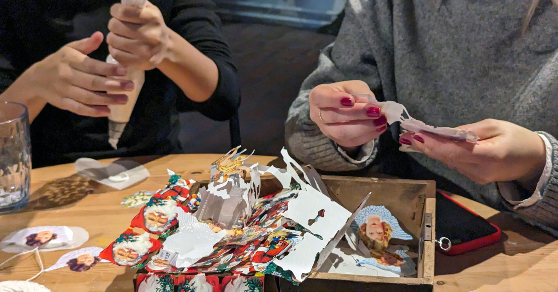руки двох жінок, що сидять за столом і займаються різдвяними ремеслами.